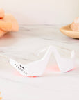 A pair of red light therapy glasses on a marble surface, with a wooden frame and a flower-like object in the foreground.