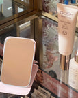 Gosh Húðvörur og lítill ferðaspegill. GOSH skincare products including a bottle and a compact mirror on a glass surface.