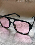Black sunglasses with pink lenses on a textured surface