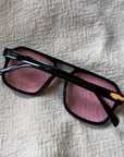 Black sunglasses with pink lenses on a textured beige surface