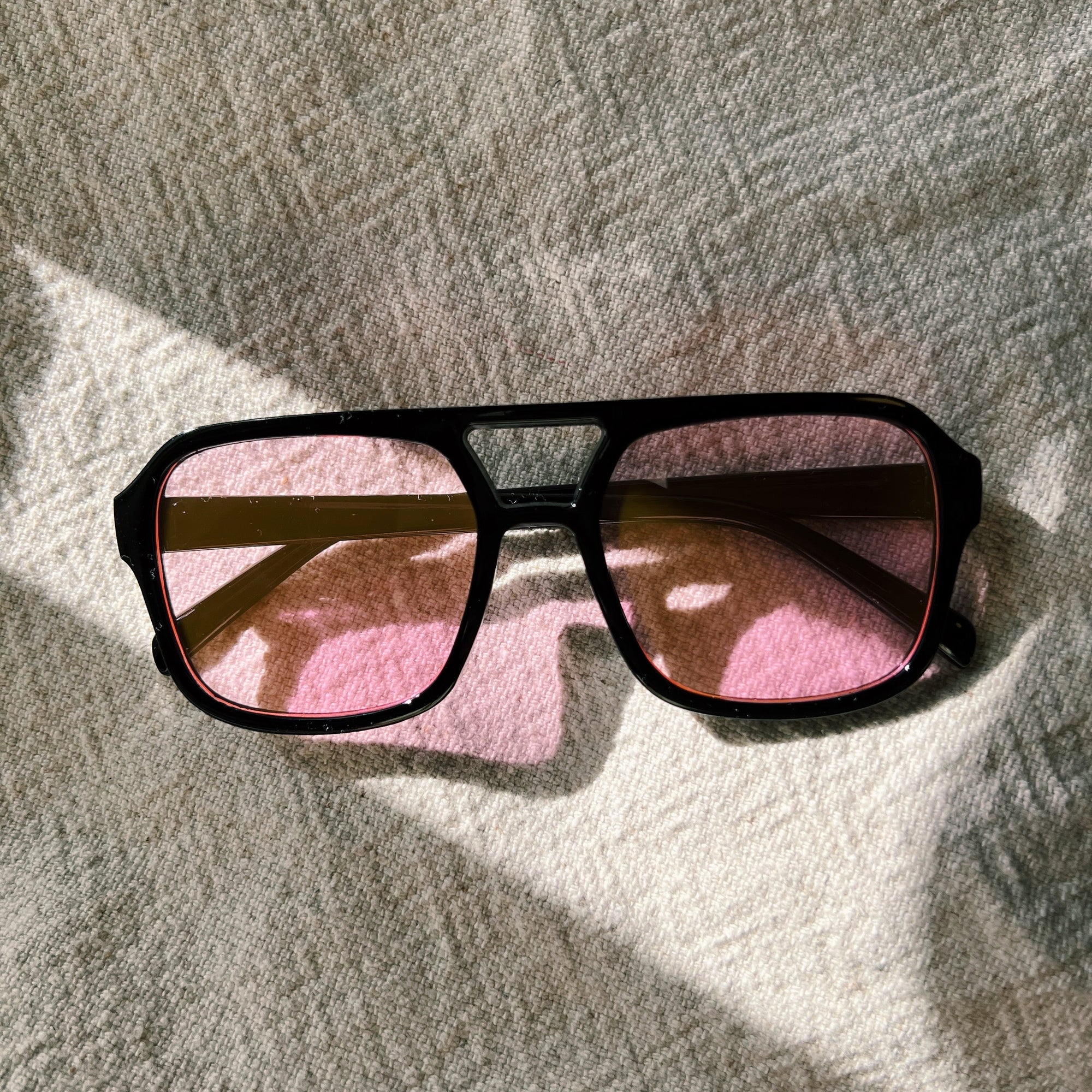 Sunglasses with pink lenses on a textured surface