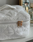 White embroidered pouch with gold zipper on a blurred background
