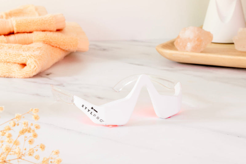 A pair of red light therapy glasses on a marble surface, with a wooden frame and a flower-like object in the foreground.