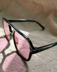 Black sunglasses with pink lenses on a textured surface