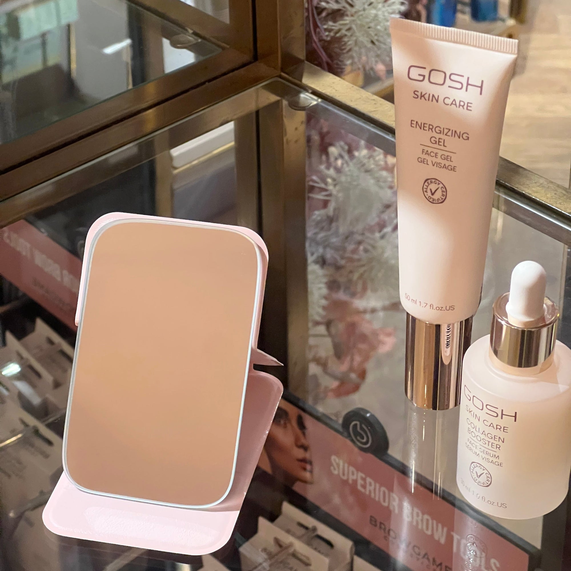 Gosh Húðvörur og lítill ferðaspegill. GOSH skincare products including a bottle and a compact mirror on a glass surface.